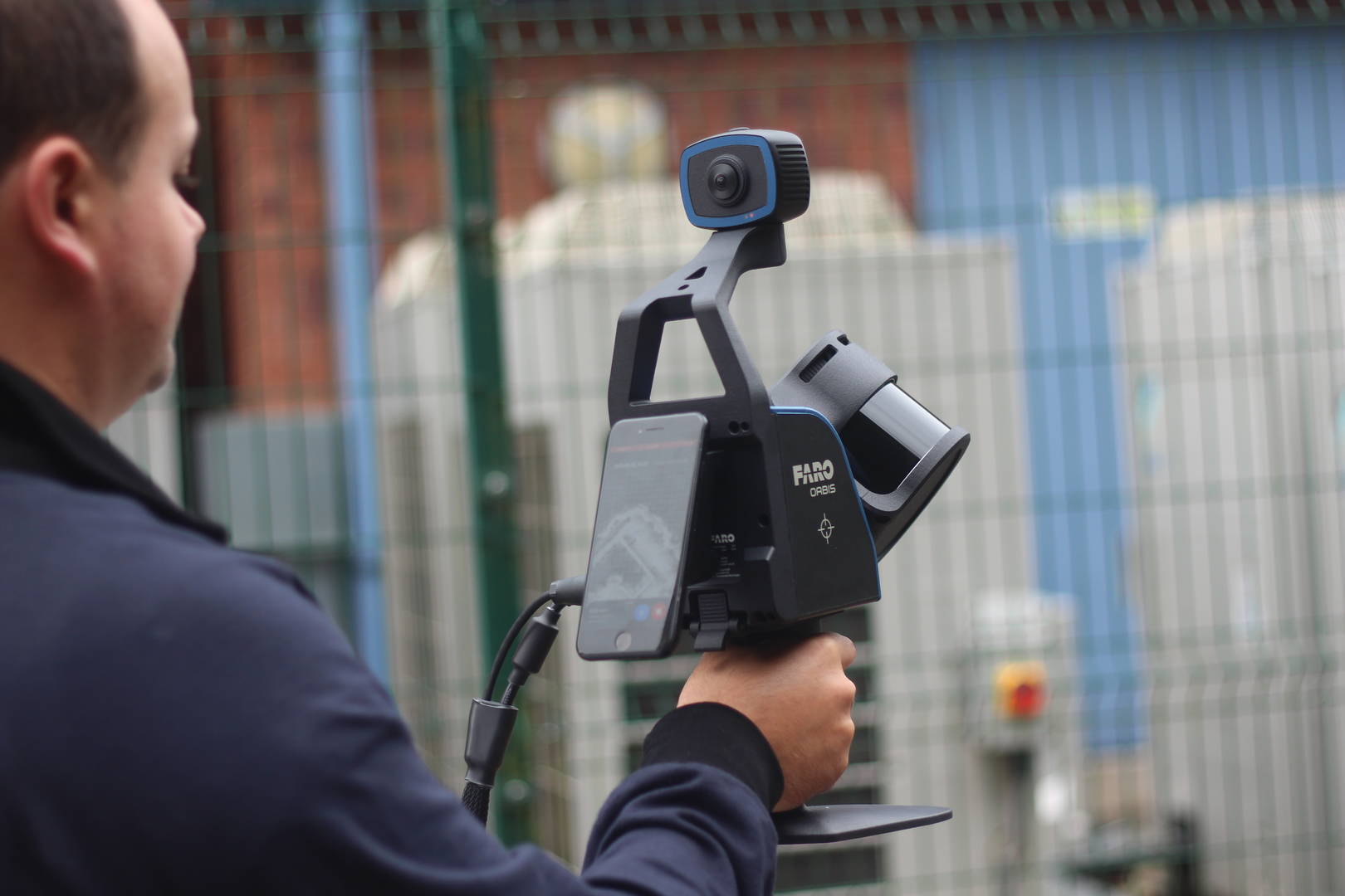 Man holding a FARO Orbis Mobile LiDAR scanner, wearing personal protection equipment outdoors