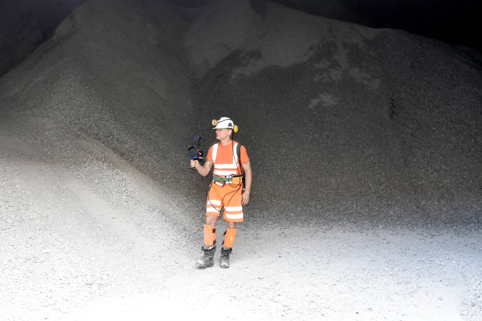 Mine surveyor wearing personal protection equipment stood in front of a stockpile, mapping using a handheld laser scanner