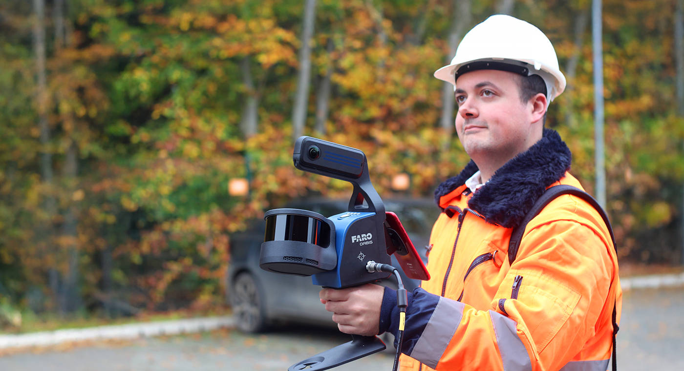 Man in personal protective gear scanning with a FARO Orbis Premium mobile scanner in an outdoor parking area