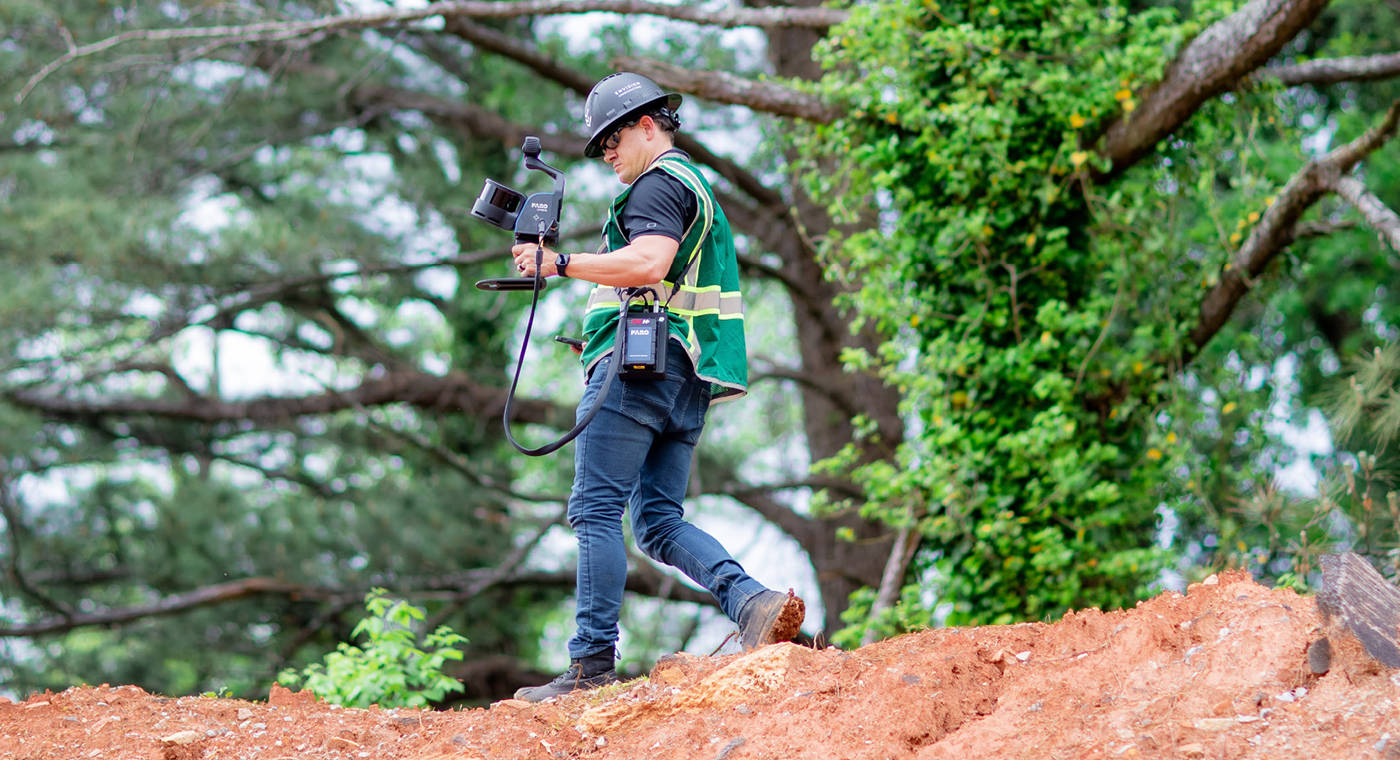 Man scanning with a FARO Orbis mobile LiDAR scanner in a wooded area
